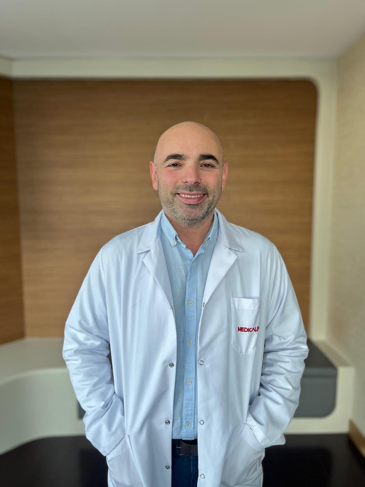 Smiling male doctor in white lab coat standing indoors with hands in pockets
