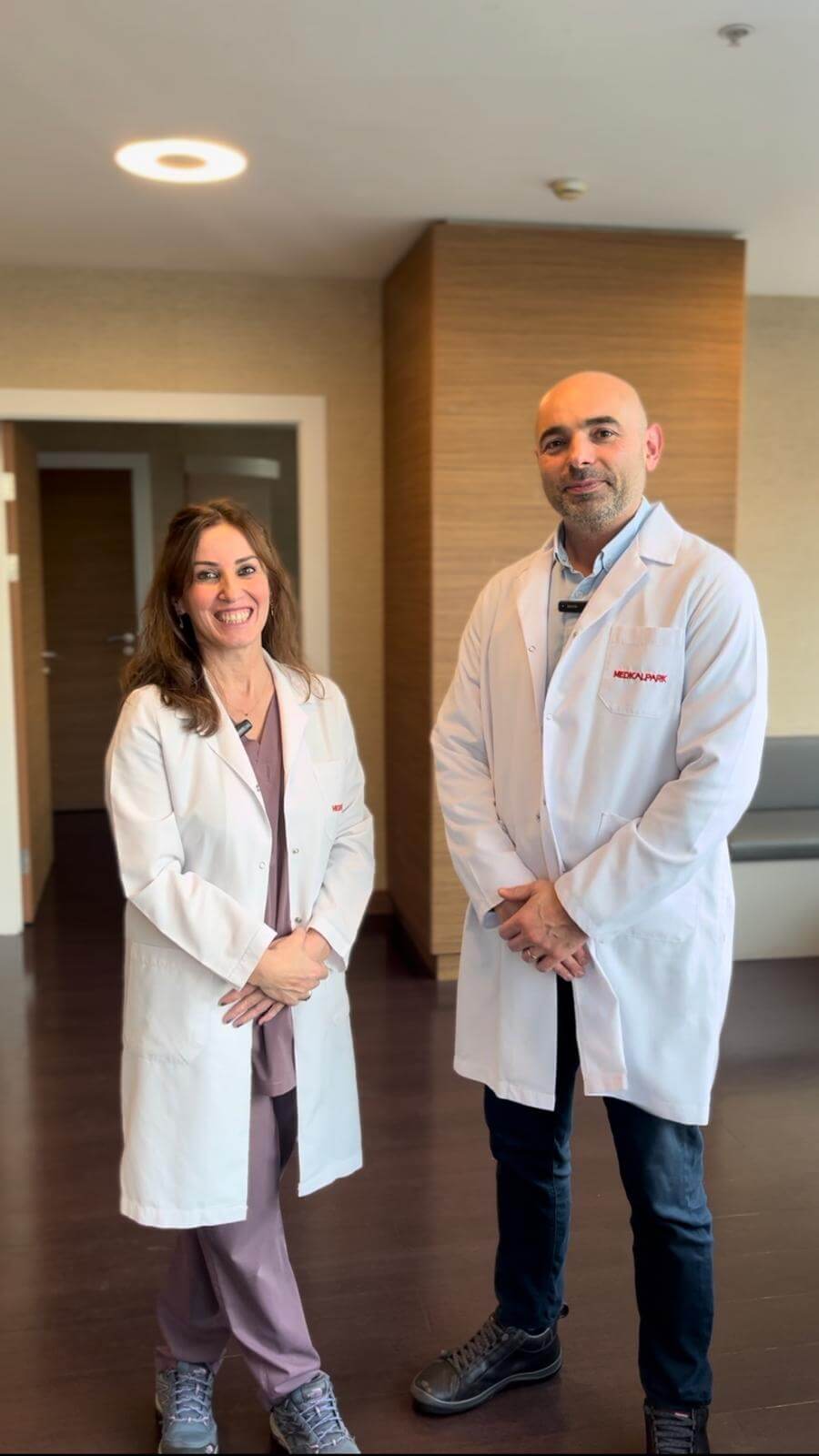 Two smiling doctors in white coats standing in a modern clinic hallway