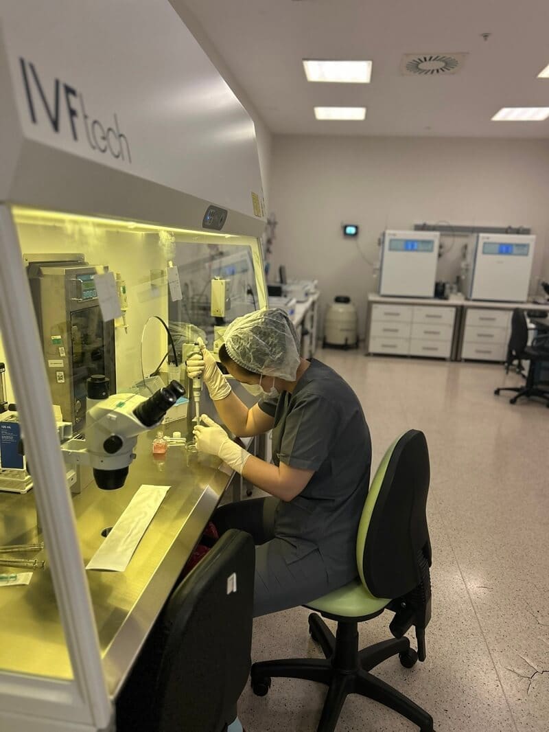 IVF lab technician working under microscope in sterile laboratory environment