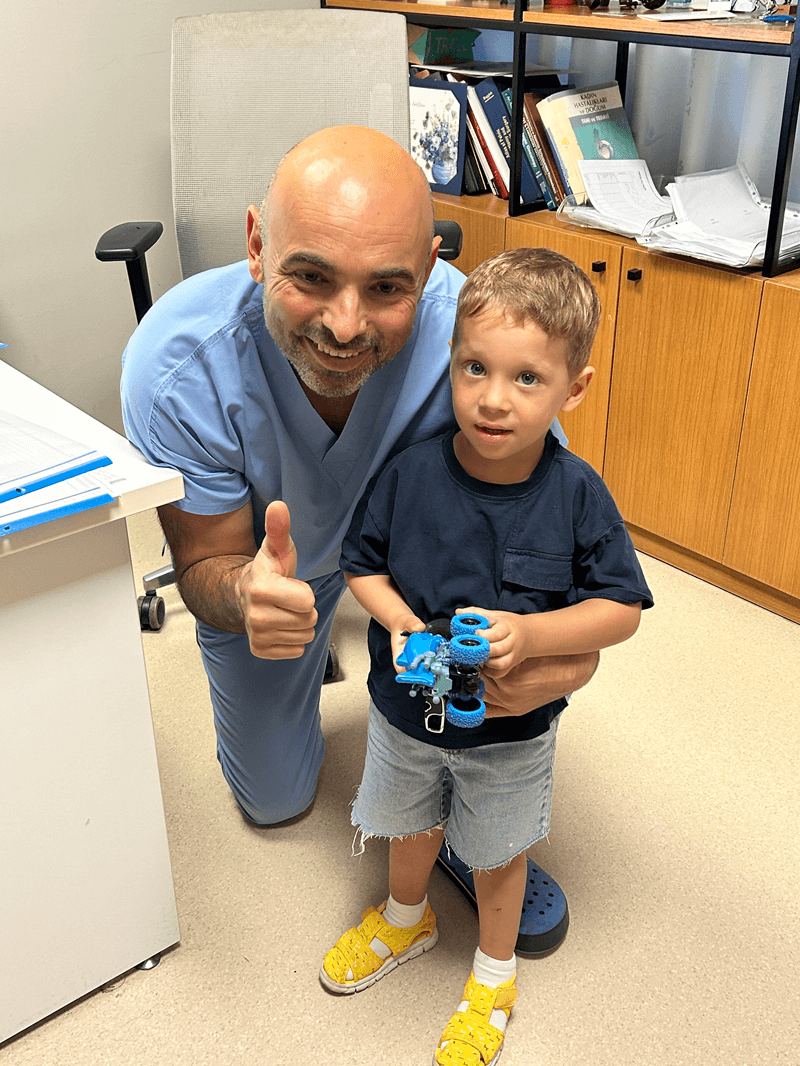 Smiling doctor giving thumbs up with young boy holding toy car in clinic office