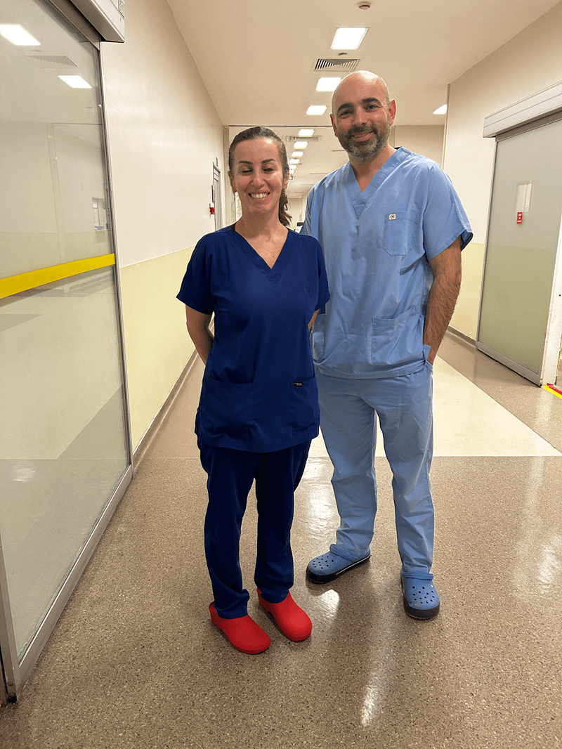 Two healthcare professionals in scrubs standing in a hospital corridor smiling